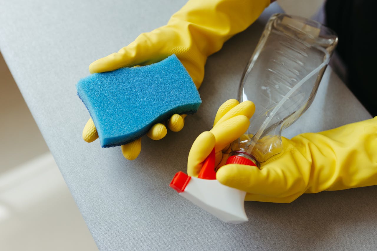 hero-img Close-up of hands in gloves holding a sponge and spray bottle for cleaning.