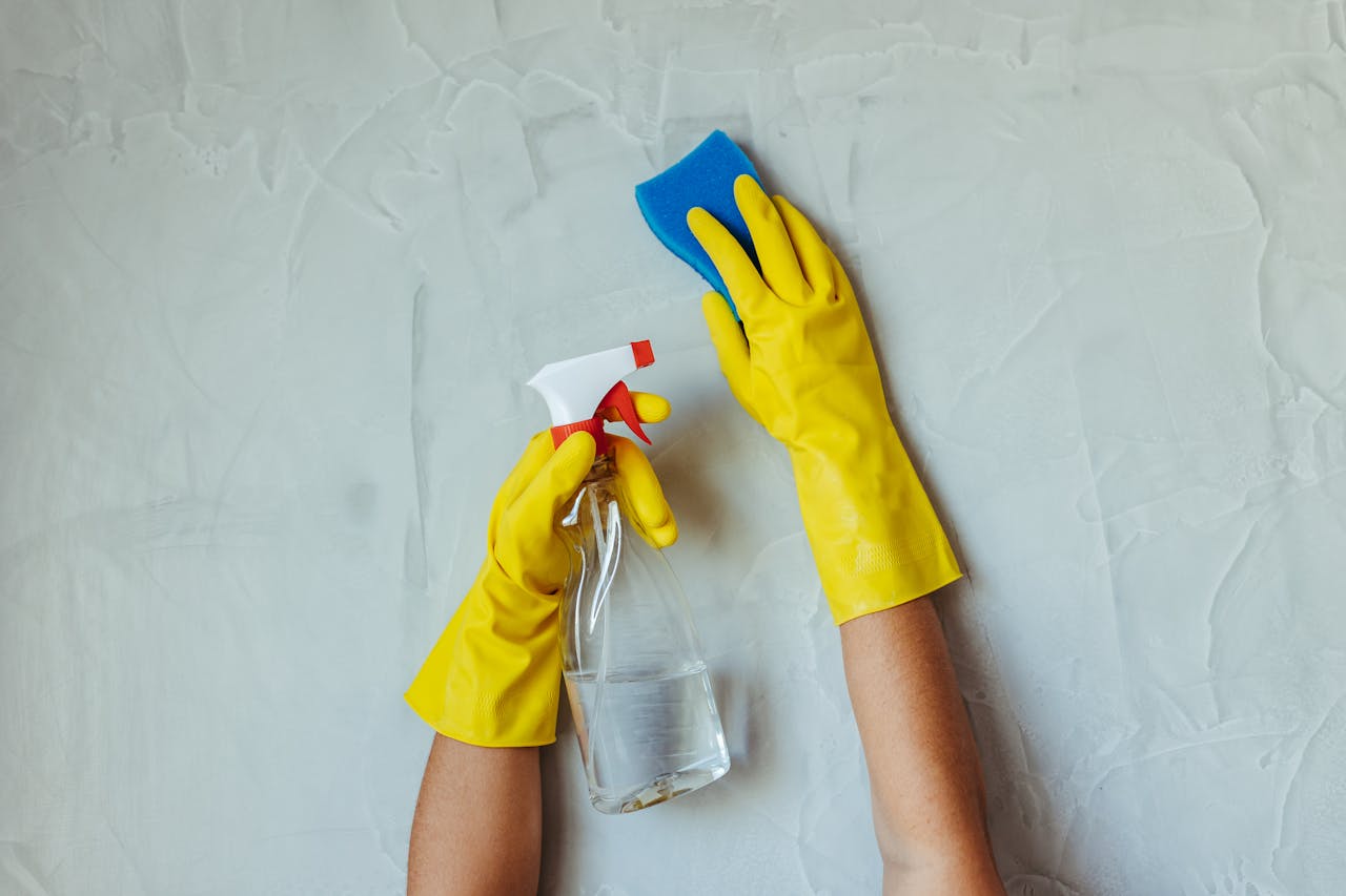 about-01 Close-up of hands in yellow gloves cleaning a wall with a spray bottle and sponge.